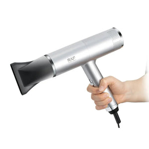 Hand holding a silver RAF professional hair dryer with nozzle attachment on white background