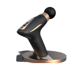 Black and gold handheld massage gun with round head on charging base, isolated on white