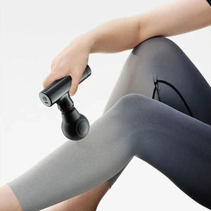 Hand using black massage gun on leg in gray leggings