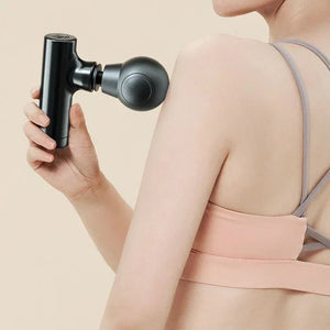 Woman using a black massage gun on shoulder, wearing sports bra, relax therapy tool