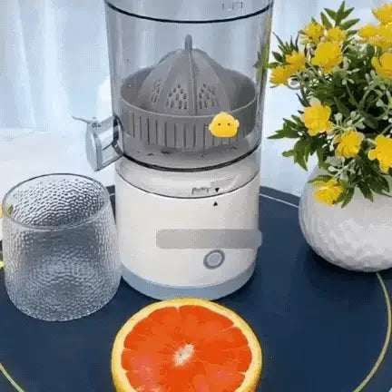 Electric citrus juicer with grapefruit, glass cup, and yellow flowers on table