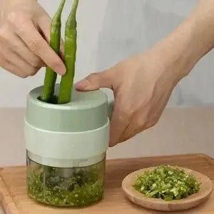 Hand using handheld rechargeable chopper to chop green chili peppers on kitchen counter