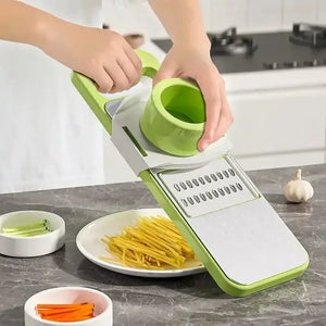 Hand using green vegetable slicer mandoline on kitchen counter with julienned vegetables