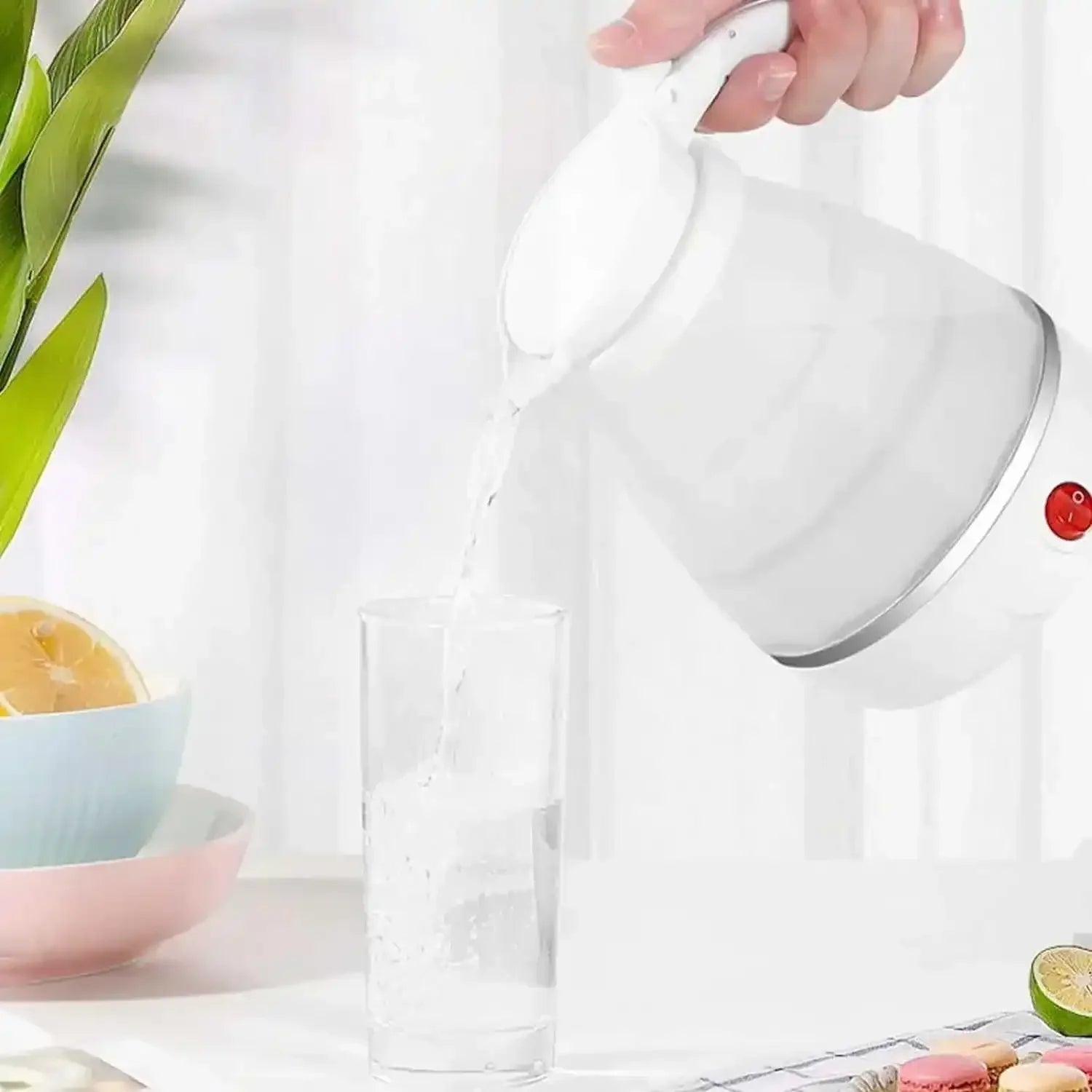 Collapsible electric kettle pouring water into glass on kitchen table with fruits and snacks