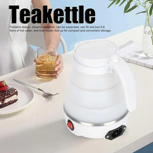 White foldable electric teakettle on table with glass of tea and dessert
