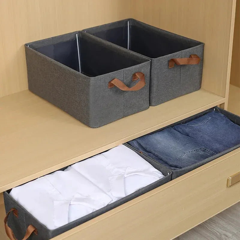 Gray fabric storage bins with leather handles in wooden closet, organizing clothes
