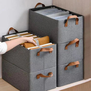 Gray fabric storage bins with handles storing folded clothes on a wooden shelf