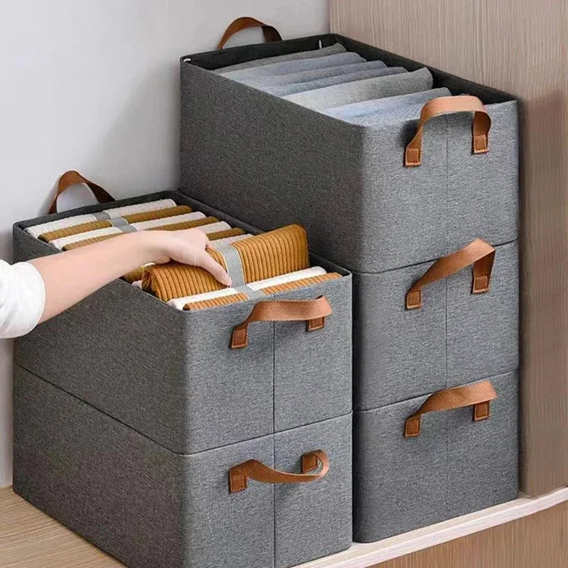 Gray fabric storage bins with handles storing folded clothes on a wooden shelf