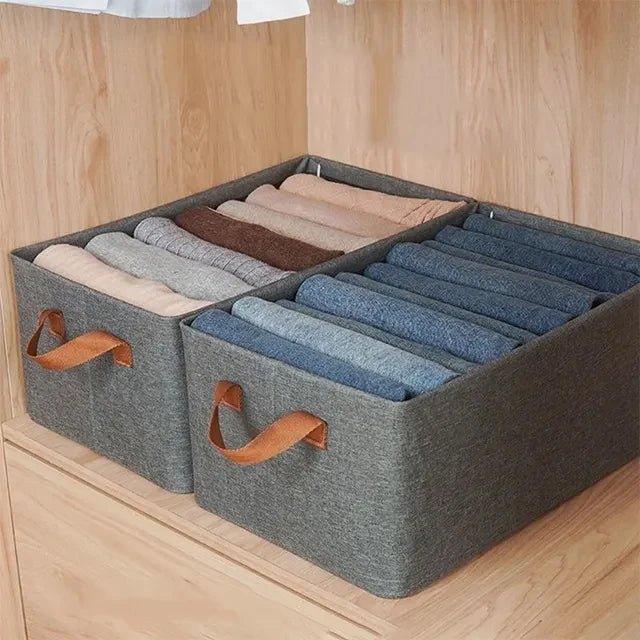 Closet storage bins with leather handles holding neatly folded clothes on wooden shelf