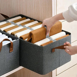 Hand organizing clothes in gray fabric storage bin with handles on wooden shelf